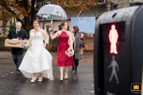 At St Marys Church in Poole, Dorset, UK, the bride is captured crossing the road just as the pedestrian signal turned red, its color matching the bridesmaid’s dress for a coordinated, candid shot taken in the rain.